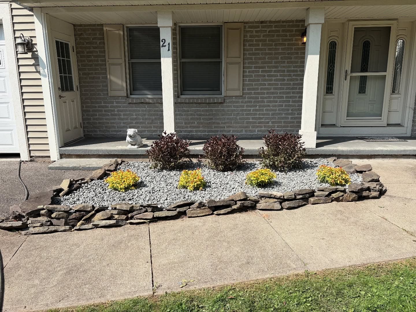 Stone border garden bed with decorative shrubs and yellow flowers